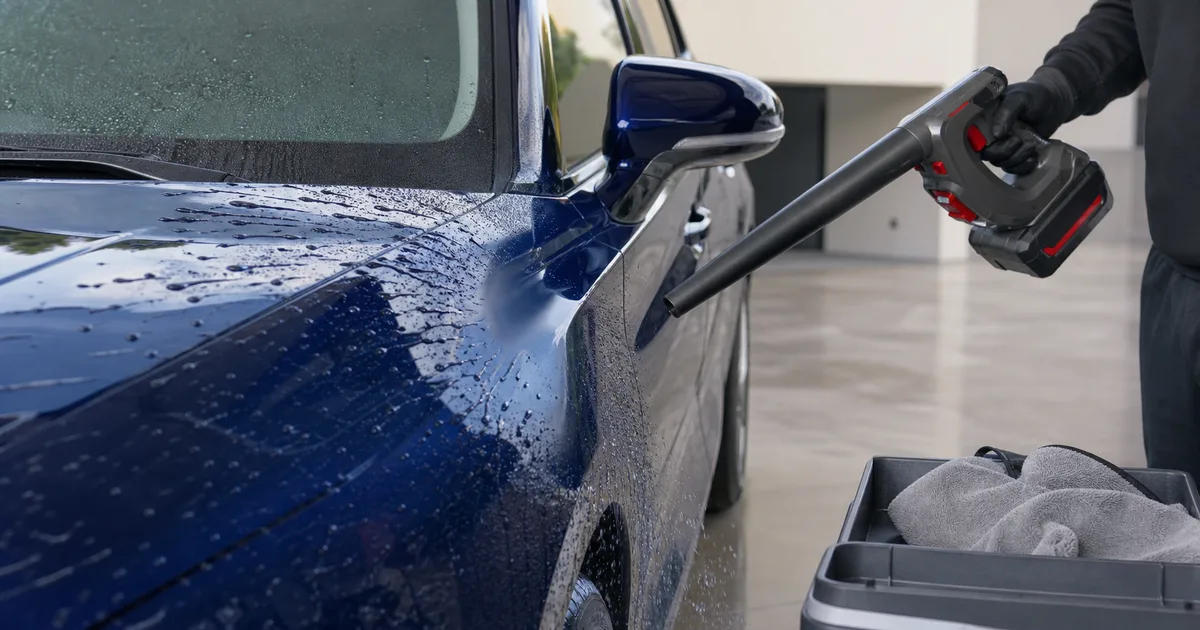 Soplador inalámbrico secando un coche azul desde distancia segura con toallas de microfibra preparadas